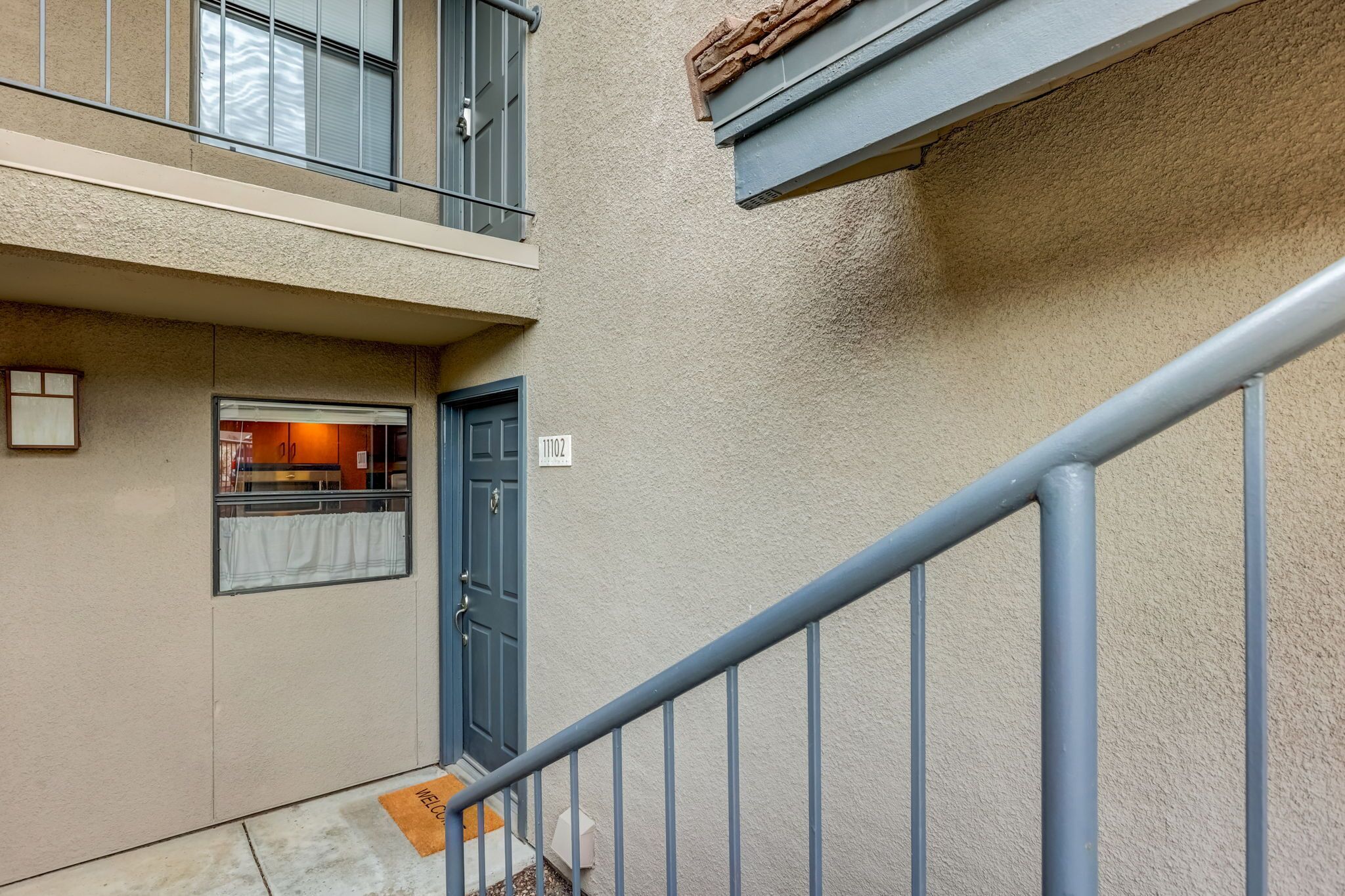 A residential building with a blue door, a balcony, and a welcome mat at the entrance.