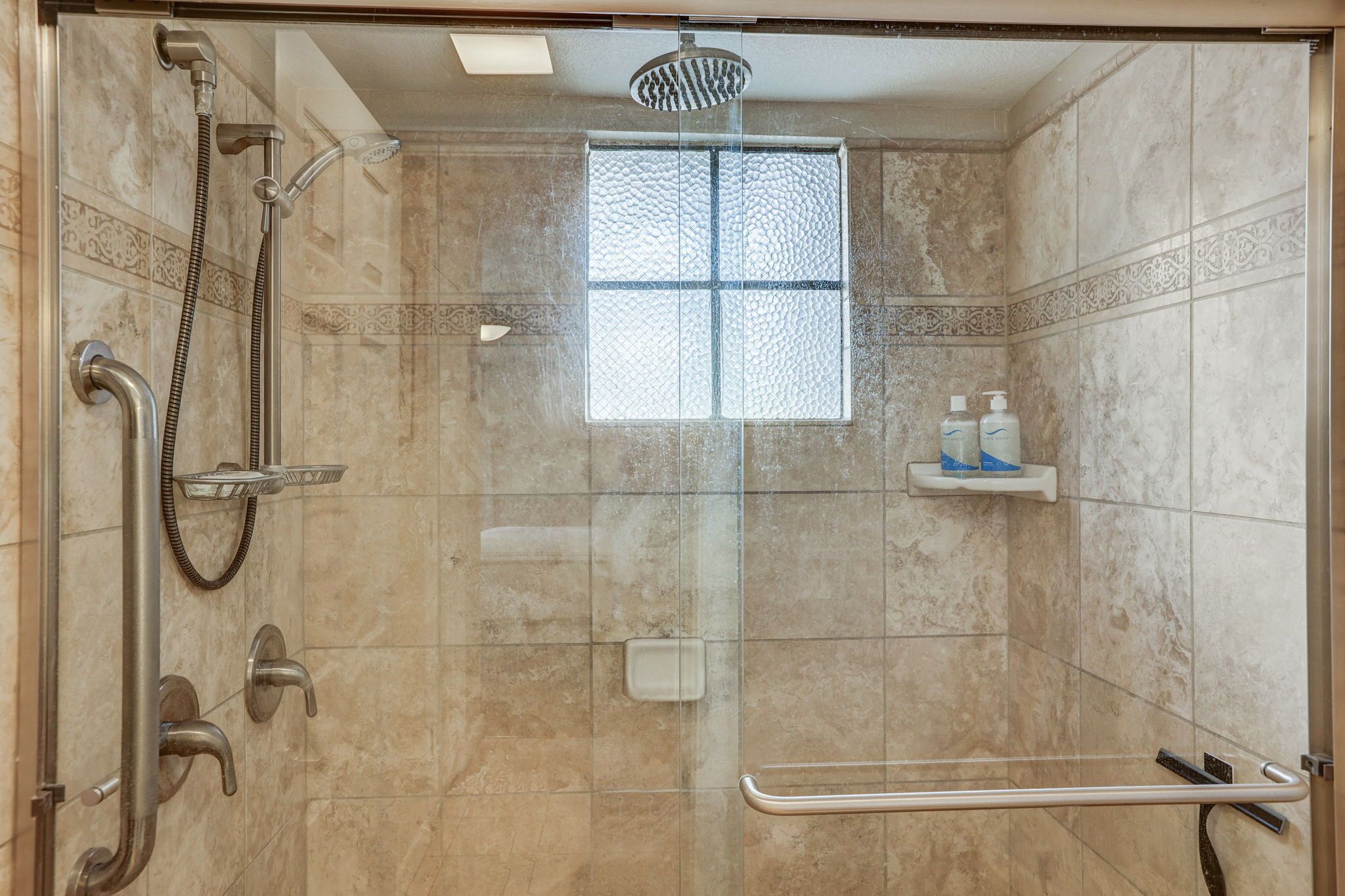A glass-enclosed shower with a handheld showerhead, a handheld shower nozzle, and a handheld shower hose.