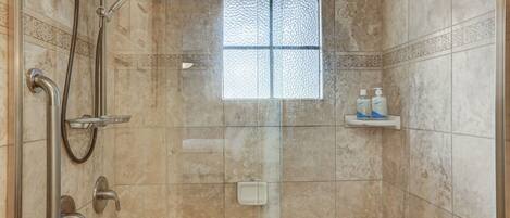 A glass-enclosed shower with a handheld showerhead, a handheld shower nozzle, and a handheld shower hose.