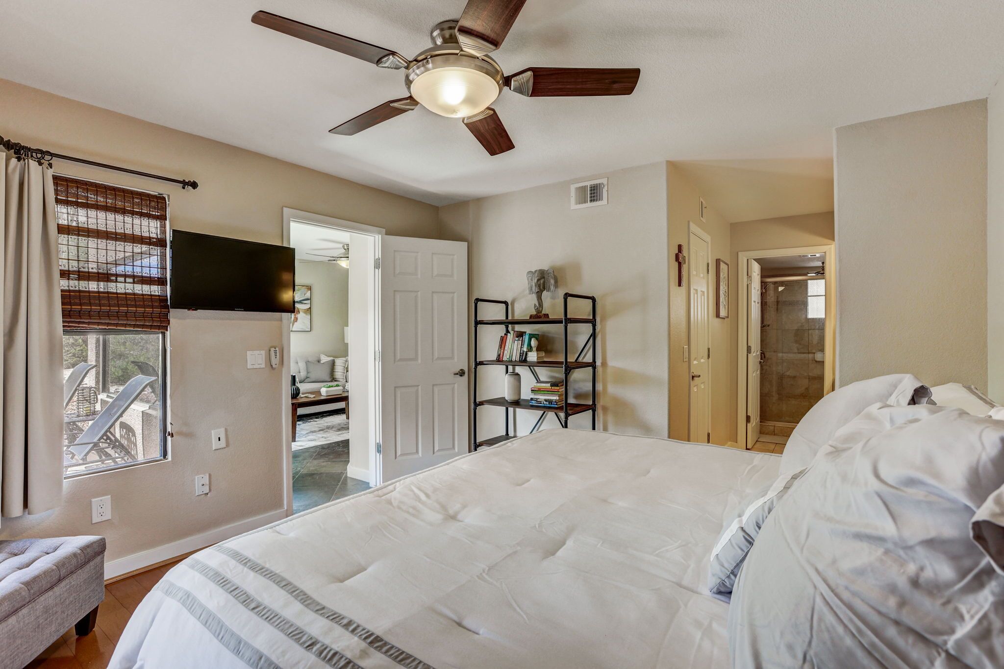 A bedroom with a large bed, a ceiling fan, a bookshelf, and a door leading to a bathroom.