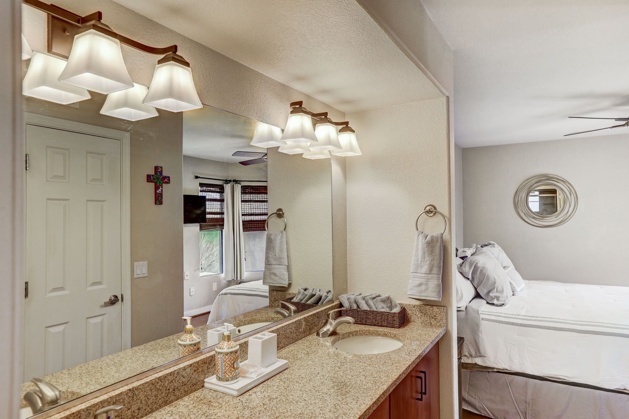 A bathroom with a large mirror, a sink, a towel rack, and a bed.