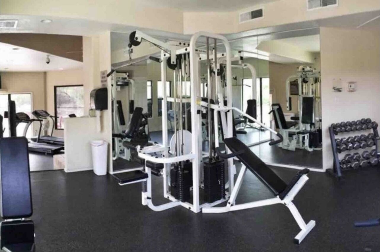 A gym with exercise equipment, mirrors, and dumbbells.