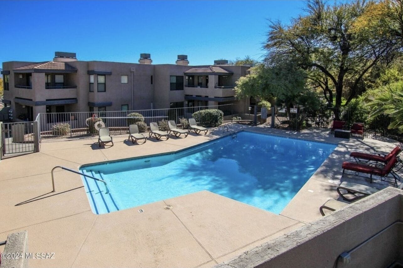 Una piscina rectangular con una escalera de metal, rodeada de sillas de descanso y una pequeña terraza.