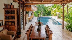 Area pranzo esterna coperta con piscina, mobili in legno e pavimento decorato.