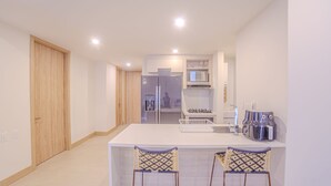 A modern kitchen with a white countertop, two bar stools, a microwave, a refrigerator, and a sink. - Exclusivo Apartamento 2Hab en Cartagena (Cartagena)