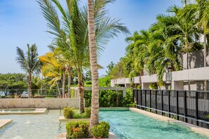 A swimming pool surrounded by palm trees and greenery, with a concrete deck and a metal fence. - Exclusivo Apartamento 2Hab en Cartagena (Cartagena)