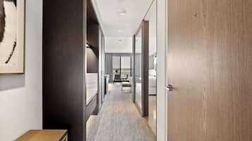 A hotel corridor with a wooden door, a framed picture on the wall, and a view into a room with a bed and a window.