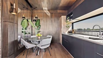 A modern kitchen with a round dining table, grey chairs, and a large window.