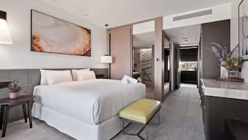 A modern hotel room with a large bed, a bedside table, a bench, a desk, and a mirror.