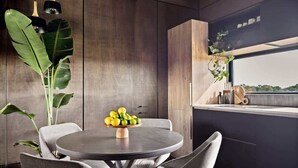 Un espace repas moderne avec une table ronde, des chaises grises et un saladier rempli de fruits.