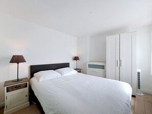 Une chambre à coucher comprenant un lit, deux tables de chevet avec des lampes, une armoire et un radiateur.