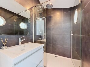 Une salle de bain moderne avec un meuble-lavabo blanc, une cabine de douche en verre et des murs recouverts de carreaux foncés.