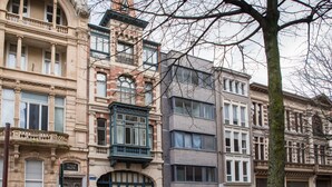 A row of historic buildings with varied architectural styles, including a building with a green balcony and a building with a black awning.