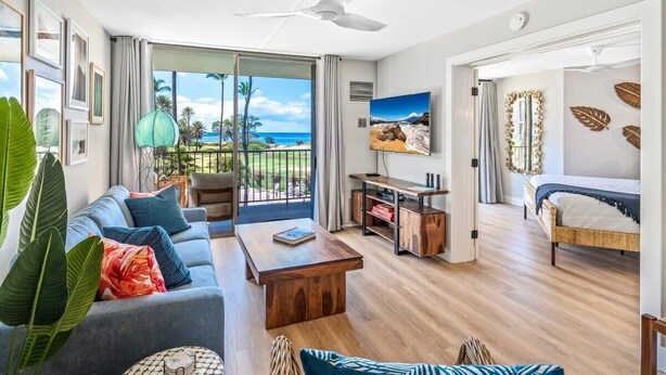 Een moderne woonkamer met een bank, salontafel en televisie, een balkon met uitzicht, en een slaapkamer met een bed en gordijnen.