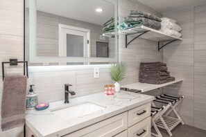 Une salle de bain moderne avec un grand miroir, un meuble-lavabo blanc, un porte-serviettes et des étagères où sont pliées des serviettes.