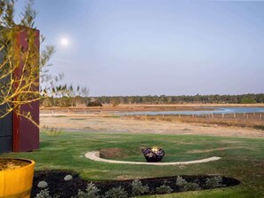 A landscaped outdoor area with a fire pit, a pond, and a building in the background.