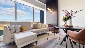 A modern living room with a sofa, chairs, a dining table, and a view of the outdoors. - Samphire Chalet Tuart—Luxury Amidst Nature (Busselton)