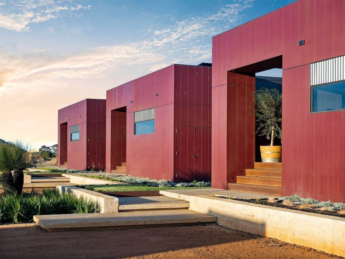 A modern building with a red facade, large windows, and a concrete pathway leading to the entrance.