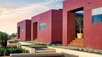 A modern building with a red facade, large windows, and a concrete pathway leading to the entrance.