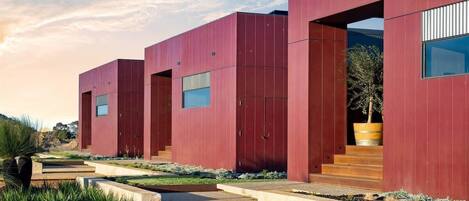 A modern building with a red facade, large windows, and a concrete pathway leading to the entrance.