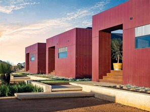 A modern building with a red facade, large windows, and a concrete pathway leading to the entrance.