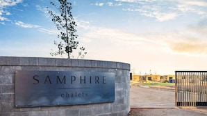 A sign for 'SAMPHIRE chalets' with a brick wall and a metal gate in the background. - Samphire Chalet Tuart—Luxury Amidst Nature (Busselton)
