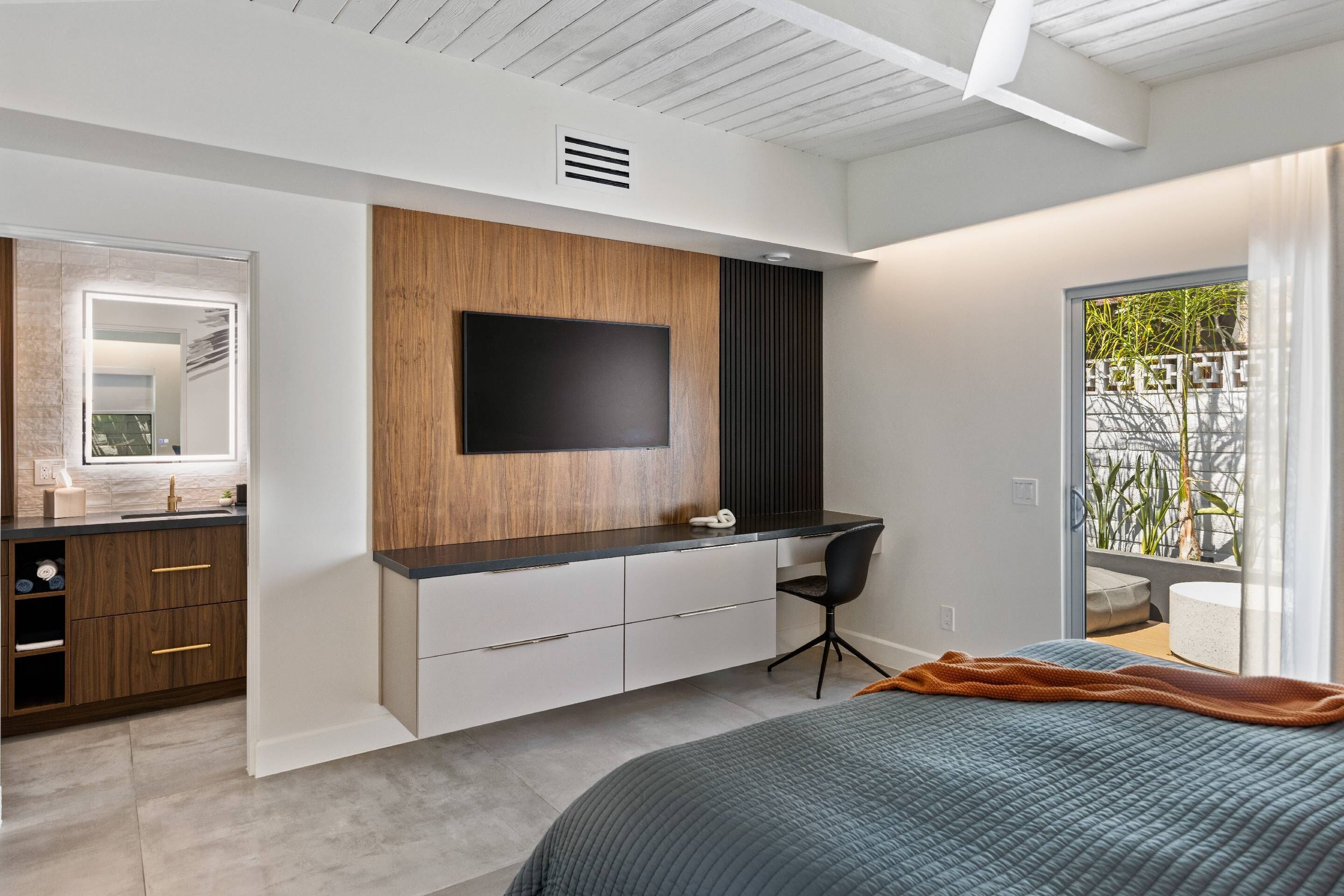 Una camera da letto moderna con un letto, una scrivania e una TV fissata al muro.