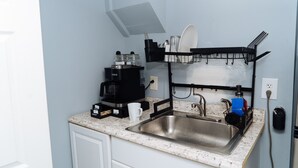 A compact kitchen with a sink, a coffee maker, and a dish rack.