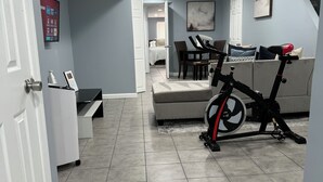 A spacious living area with a large couch, a dining table, and a stationary bike.
