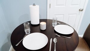 A round dining table with white plates, silverware, a candle, and a tissue roll.