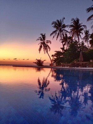 A pool reflecting palm trees and a sunset. - ABWonderdive Beach Resort (Kubu)
