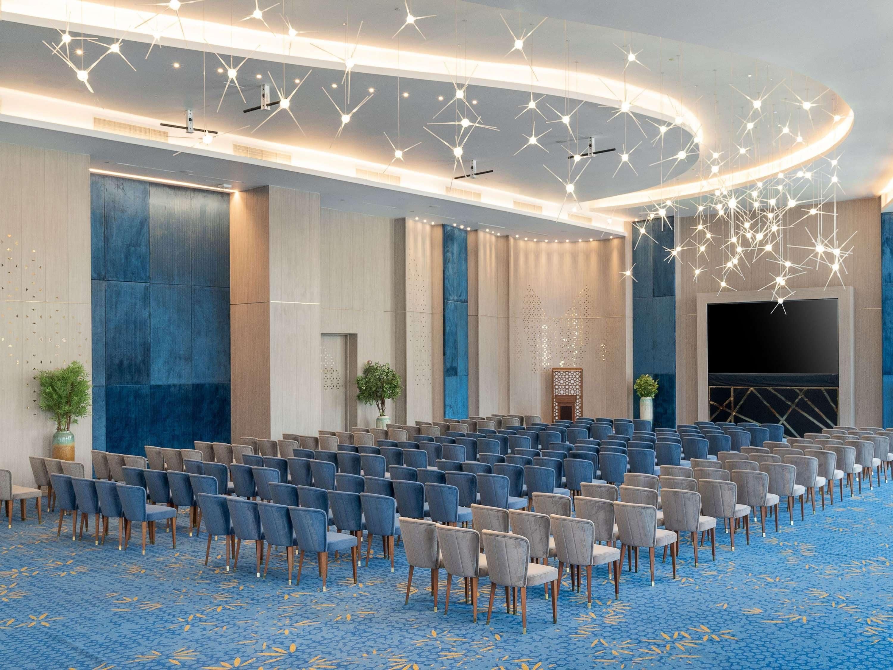 A large conference room with rows of chairs, a stage, and modern lighting fixtures.