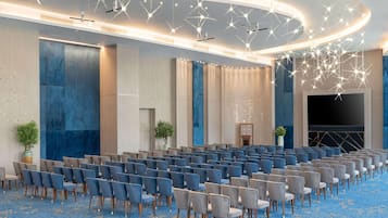 A large conference room with rows of chairs, a stage, and modern lighting fixtures.