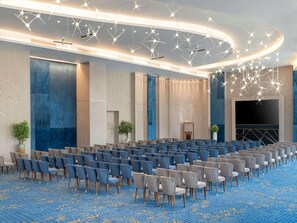 Ampia sala conferenze con file di sedie, un palco e moderne lampade.