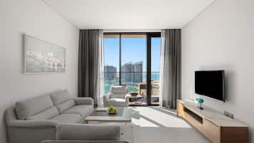 A modern living room with a grey sofa, a coffee table, a TV, and a view of the city and sea.