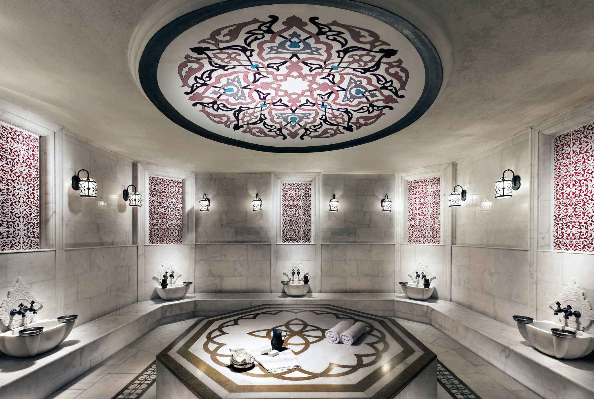 Casa de banho luxuosa com design circular central, várias lavatórios e painéis decorativos na parede.