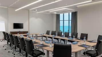 A conference room with a long table, black chairs, water bottles, and a TV on the wall.