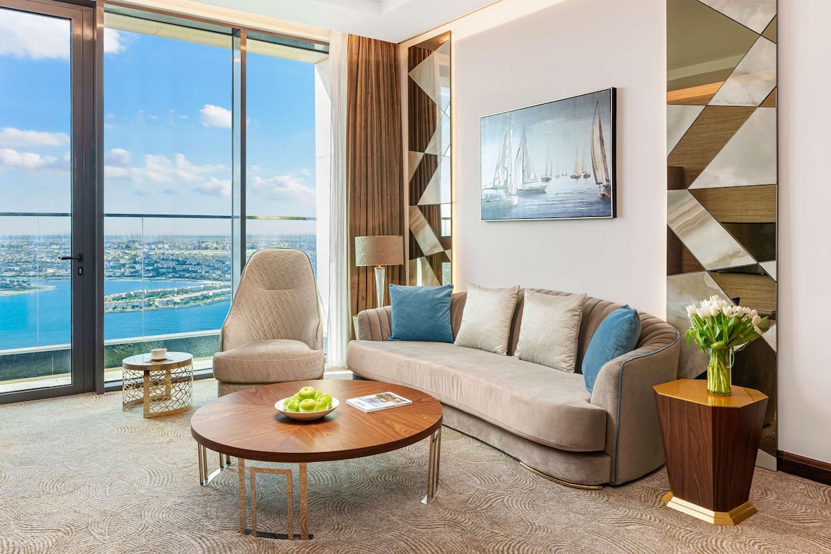 Un salon moderne avec un canapé, une table basse et une vue sur la ville grâce à de grandes fenêtres.