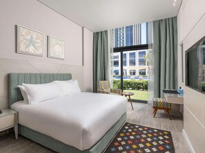 Een moderne hotelkamer met een groot bed, een bureau, een stoel en uitzicht op de stad door grote ramen.