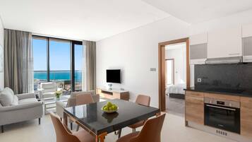 A modern hotel room with a dining area, a kitchen, and a large balcony with a sea view.