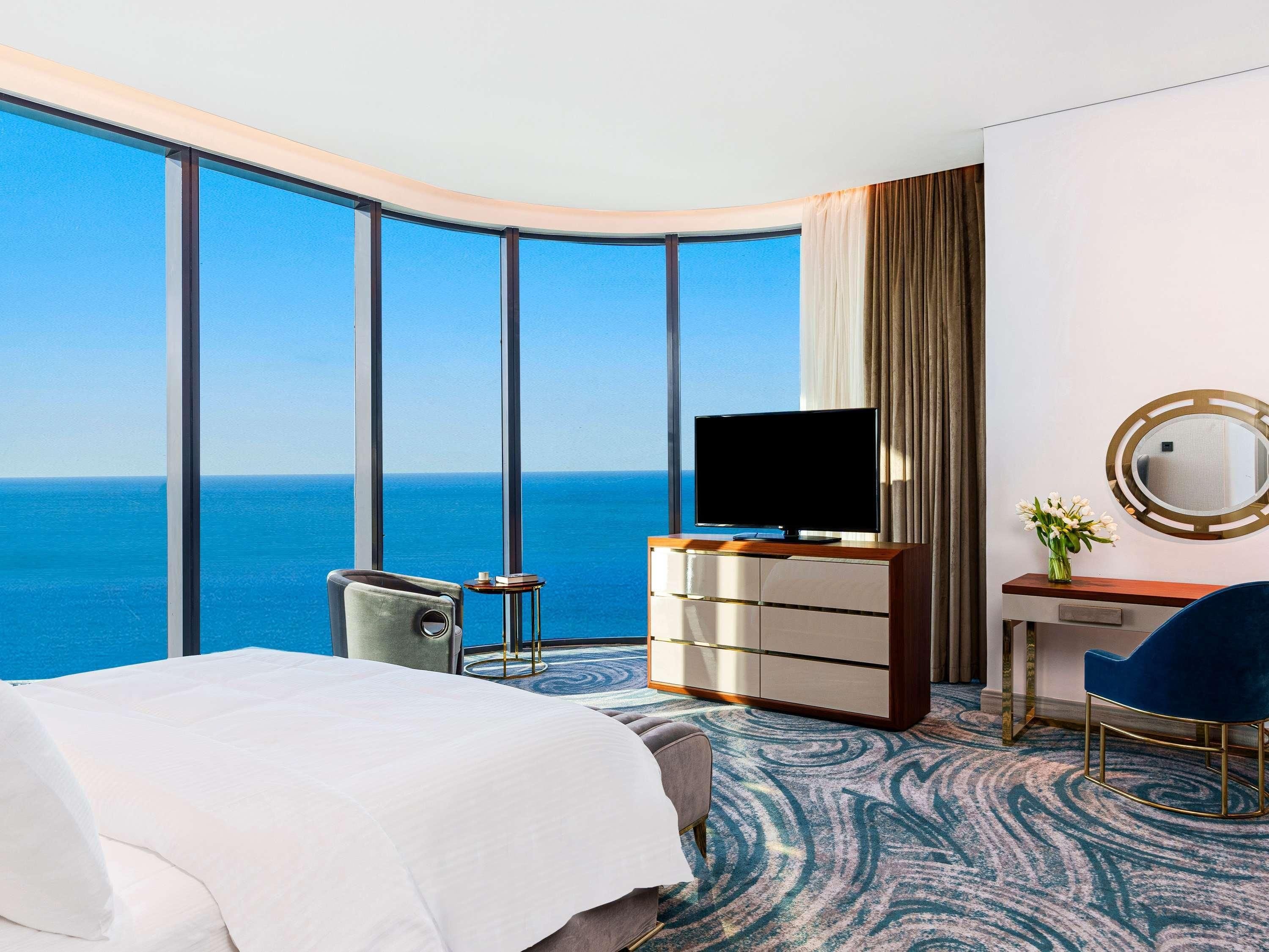 Een hotelkamer met een groot raam, een bed, een bureau met een televisie en een stoel.