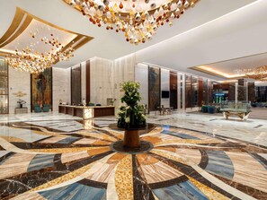 A spacious lobby with a central reception desk, a large decorative plant, and a patterned floor. - Rixos Premium Alamein (El Alamein)