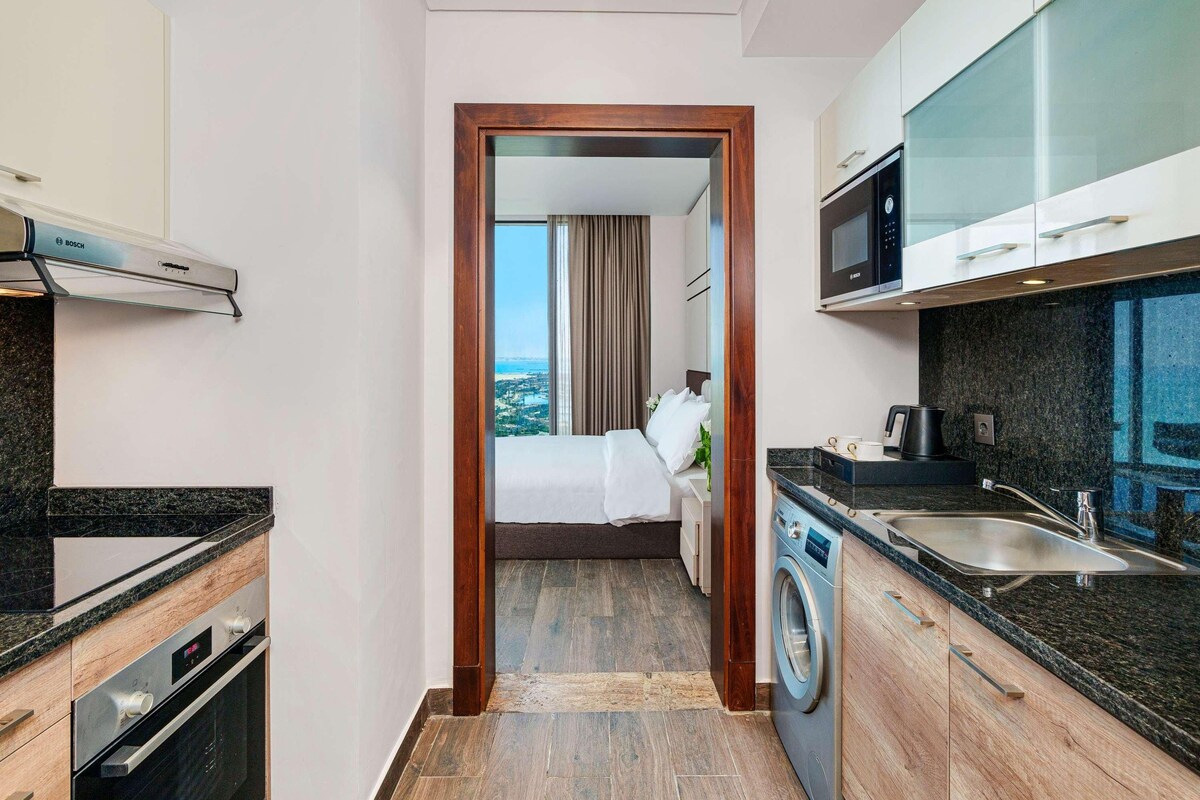 Ein kompaktes Hotelzimmer mit Küchenzeile, einer Waschmaschine und einem Bett mit Blick auf die Stadt.