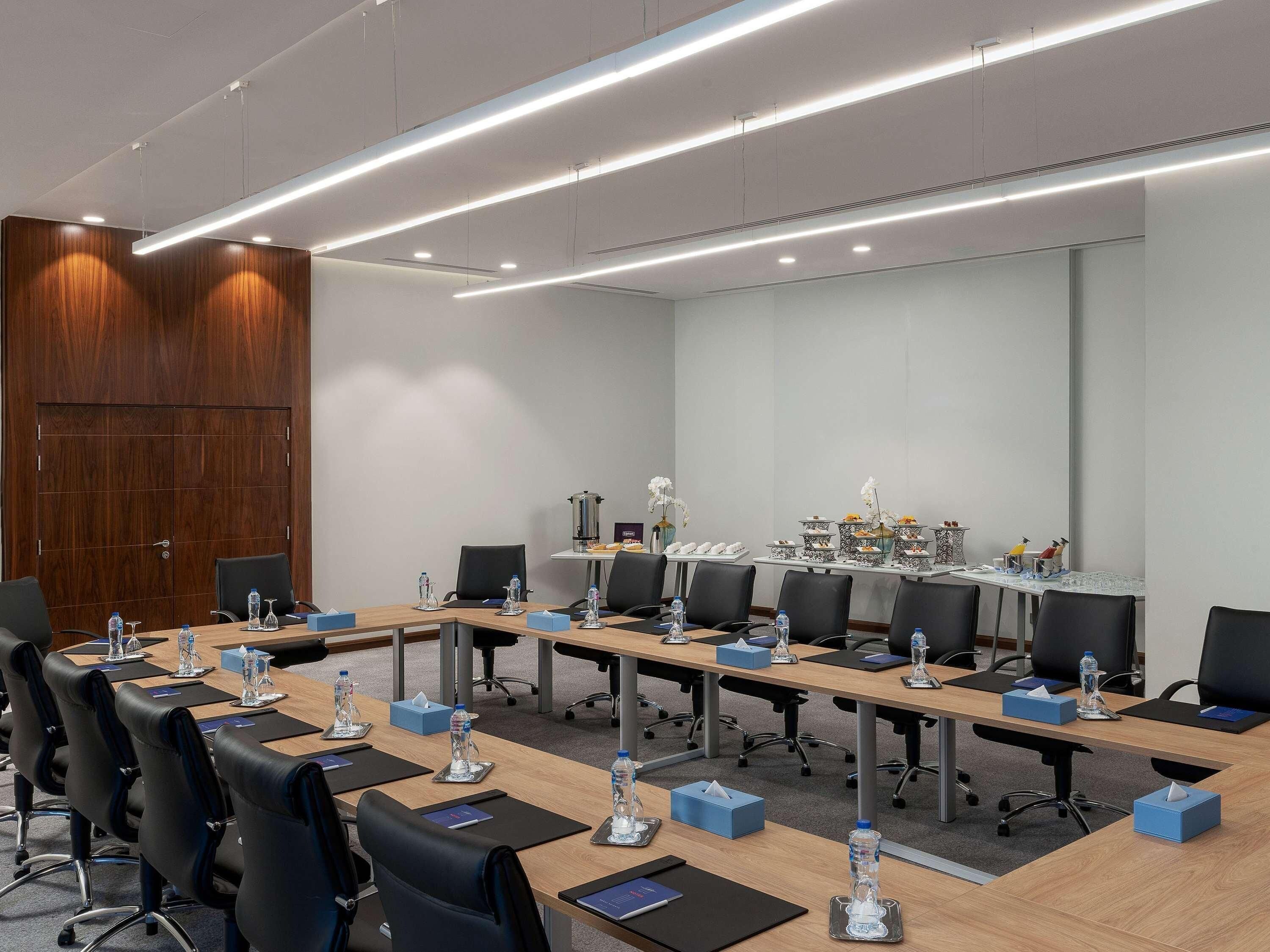 A conference room with long tables, black chairs, water bottles, and tissue boxes.