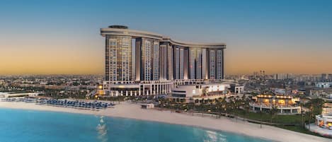 A high-rise hotel with a beachside location, featuring multiple floors, a pool area, and a well-lit facade.