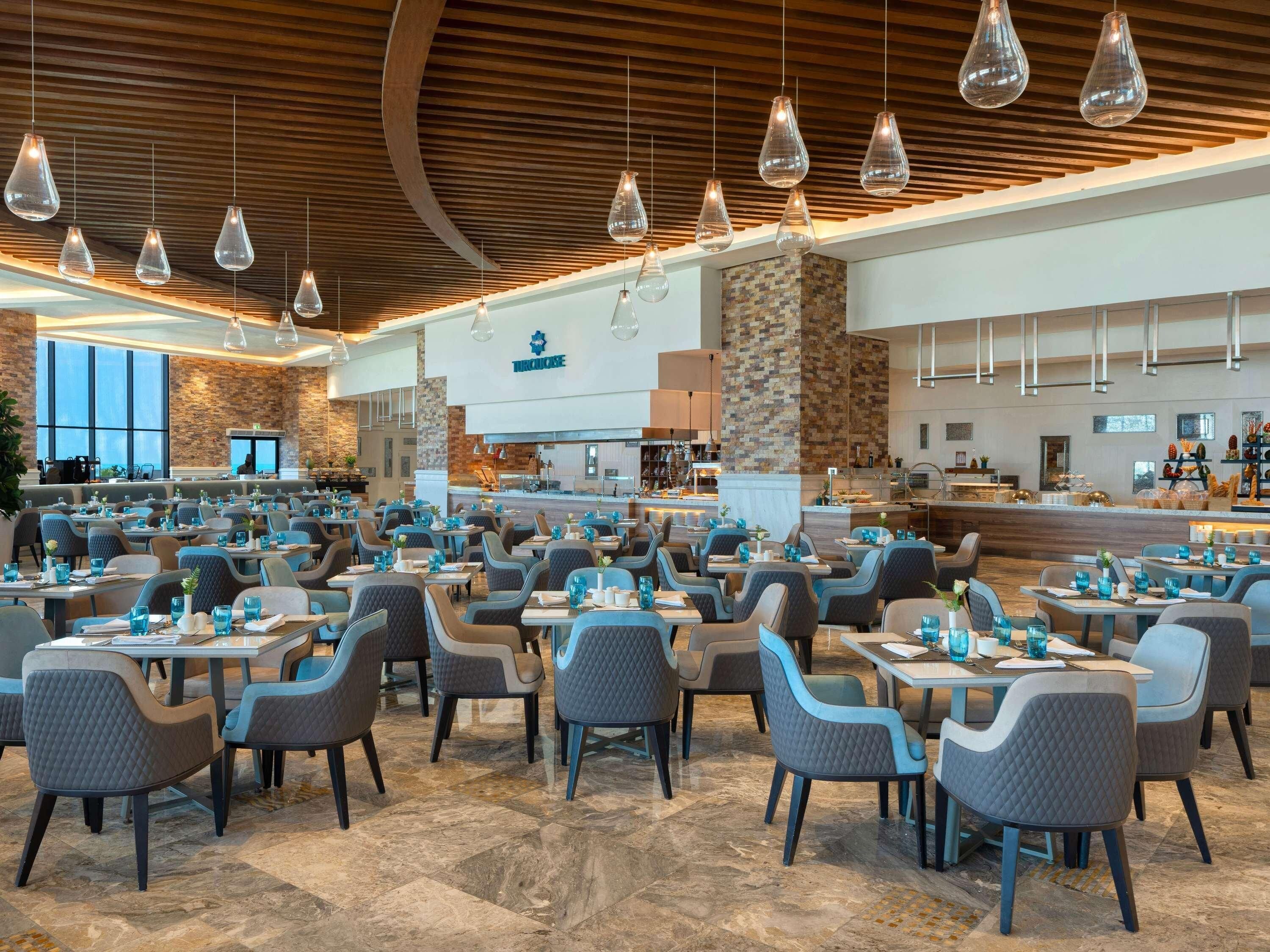 A spacious restaurant with multiple tables and chairs, a stone wall, and hanging pendant lights.