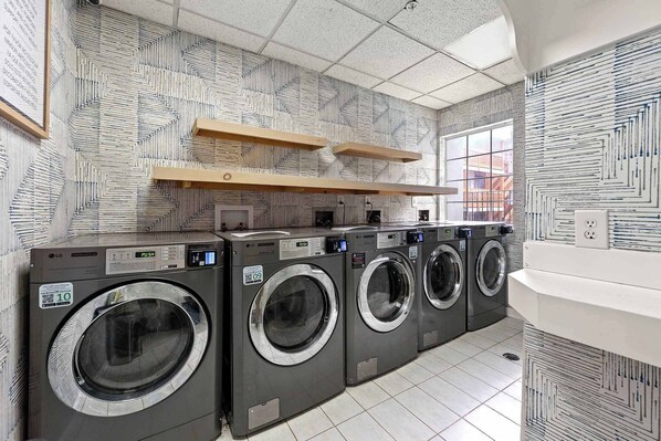 Un cuarto de lavandería con cuatro lavadoras, estantes de madera y paredes con diseño.