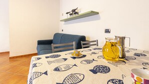 Ein Essbereich mit einem Tisch für zwei Personen, einem blauen Sofa und einem an der Wand montierten Regal mit einem dekorativen Gegenstand.