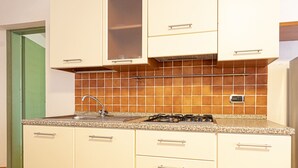 Eine Küche mit einer Granitabdeckung, einer Edelstahlspüle und einem Gasherd. Es gibt vier Schränke mit Griffen und eine Rückwand aus orangefarbenen Fliesen.