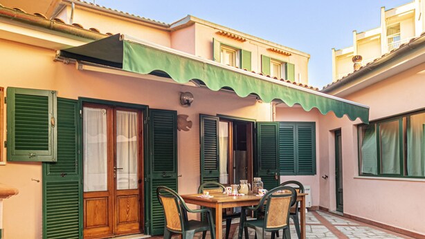 Eine Terrasse mit Tisch und Stühlen, einer Holztür und grünen Fensterläden.